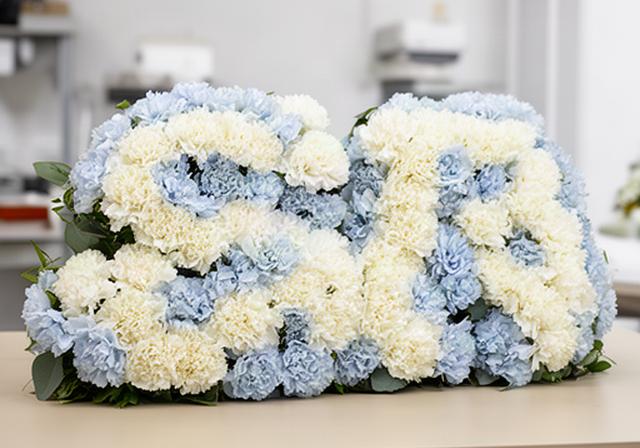 Floral letter tribute made with white carnations and pale blue flowers on a display table