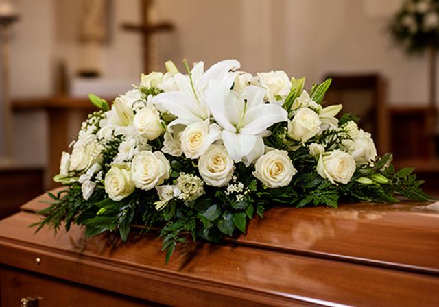 White rose and lily coffin spray resting on a polished wooden casket